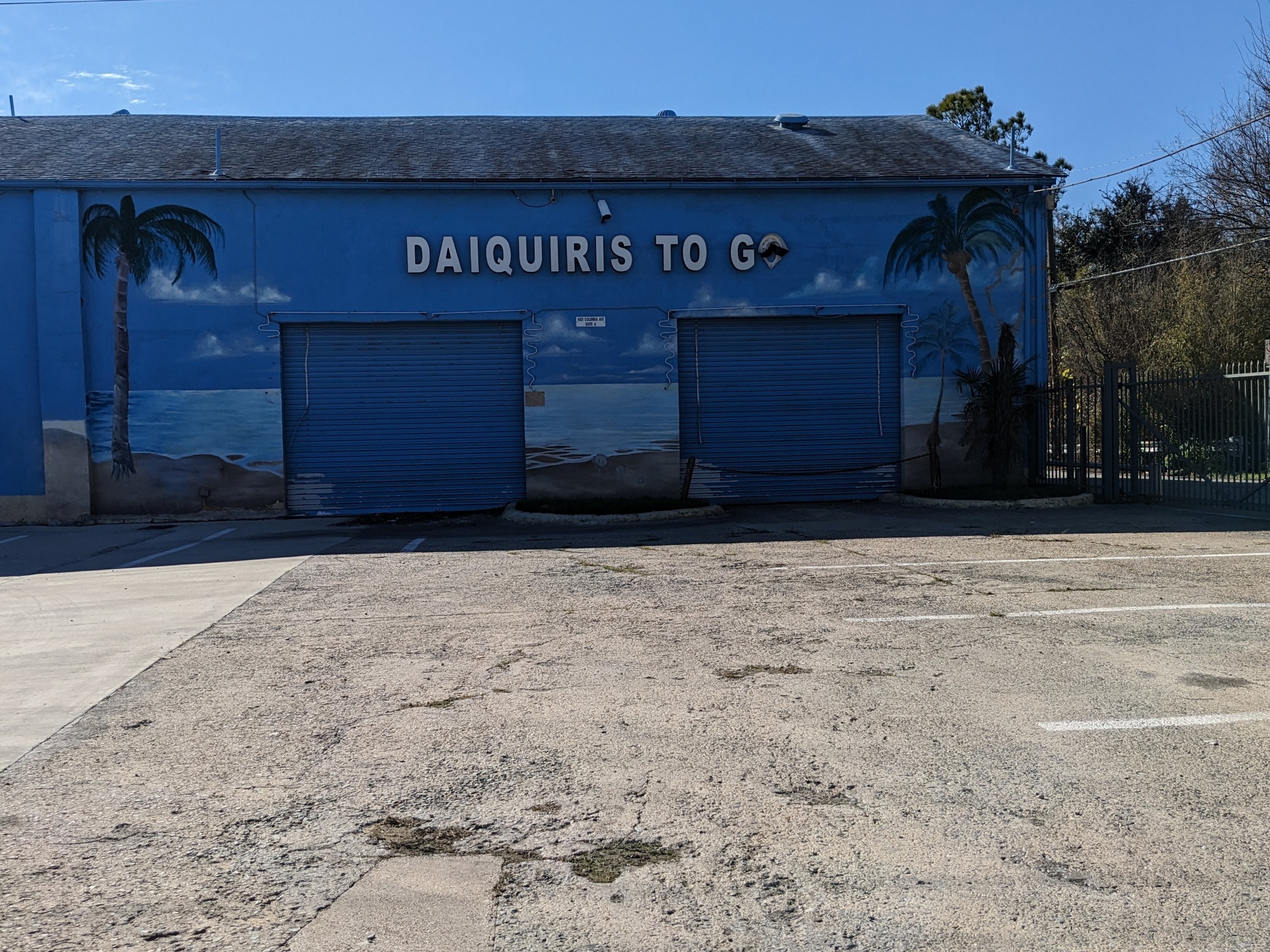 I picture of a warehouse-sized drive-through daiquiri place in East Dallas, TX, USA, called "Daiquiris to go". The "o" in "go" is half missing.