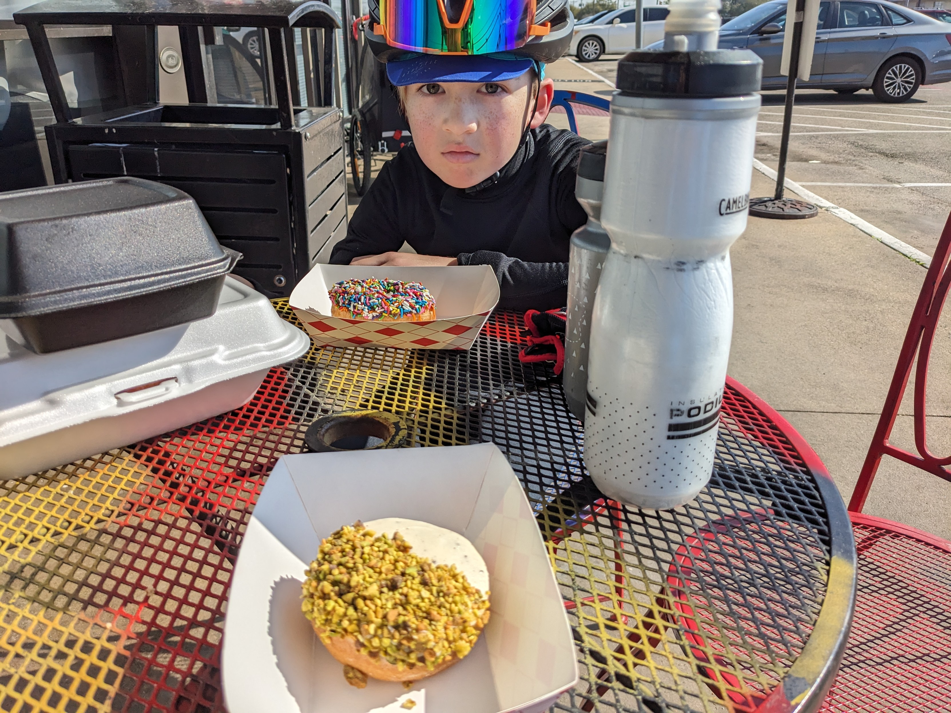 A child in cycling kit sitting at an outdoor table with a donut