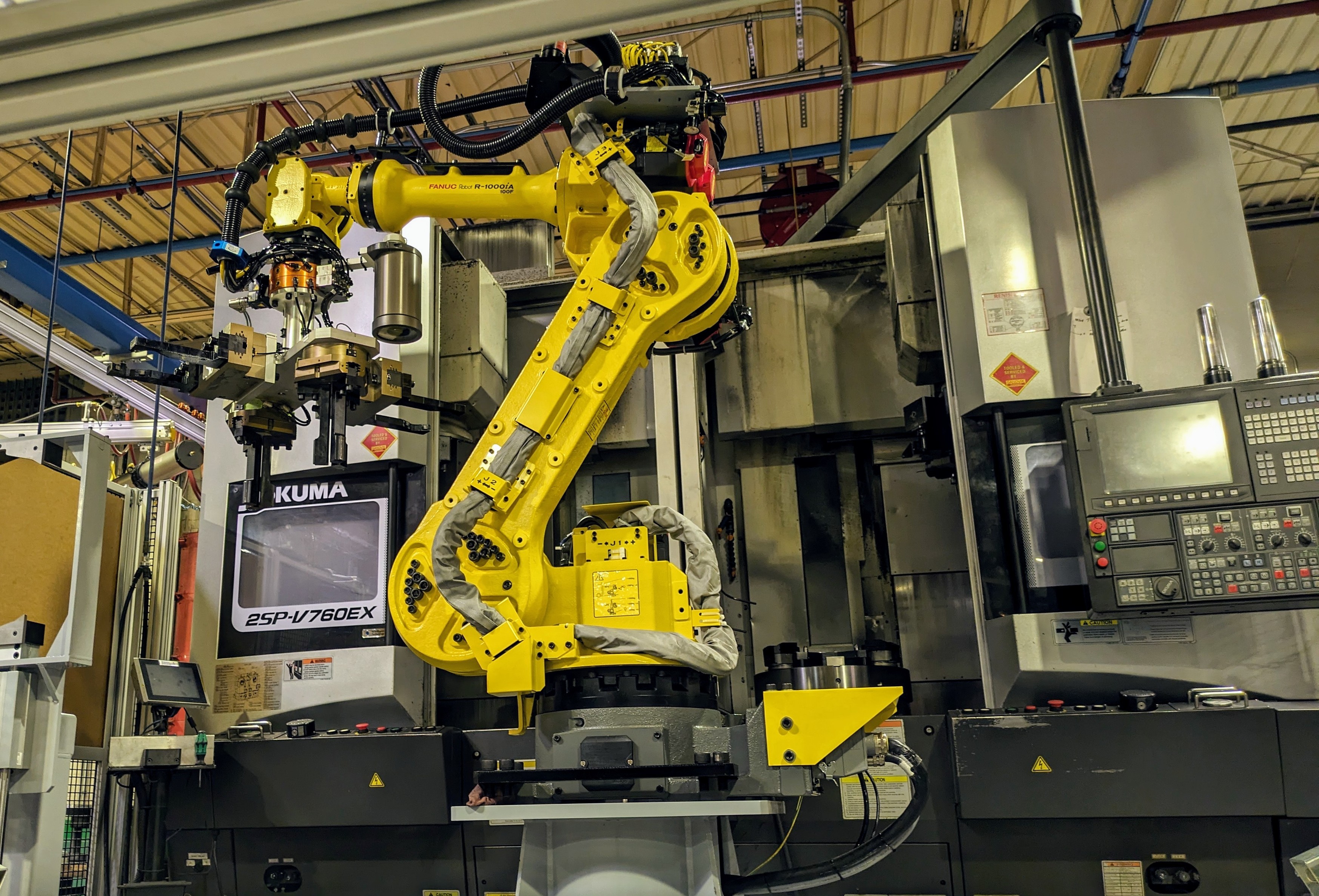 A yellow robot in front of the machining equipment it loads and unloads automatically (after a lot of specialized programming and testing)