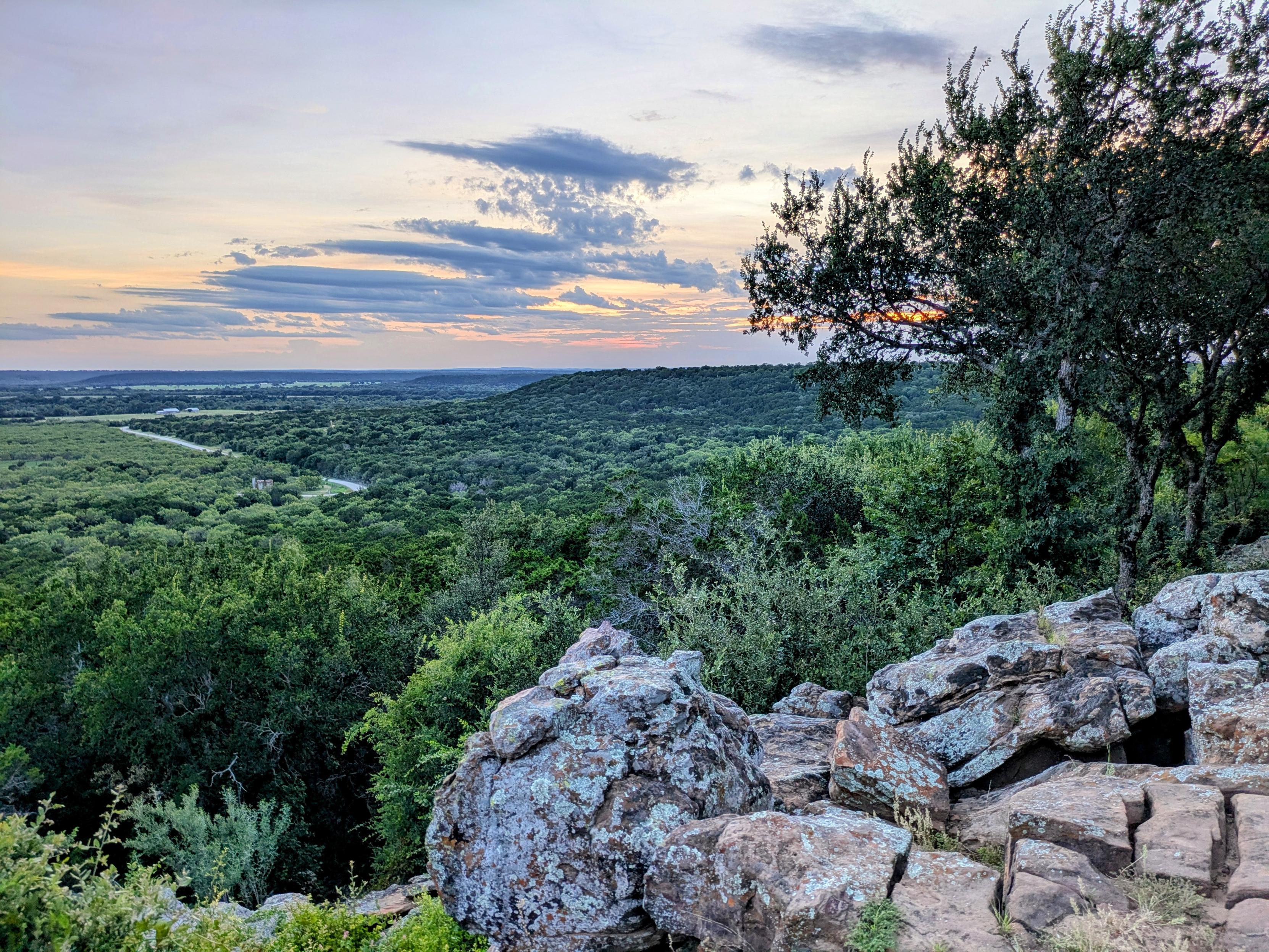 From a hill in TX. Just green to the horizon with clouds and sunset colors, some grey and red rocks in the foreground