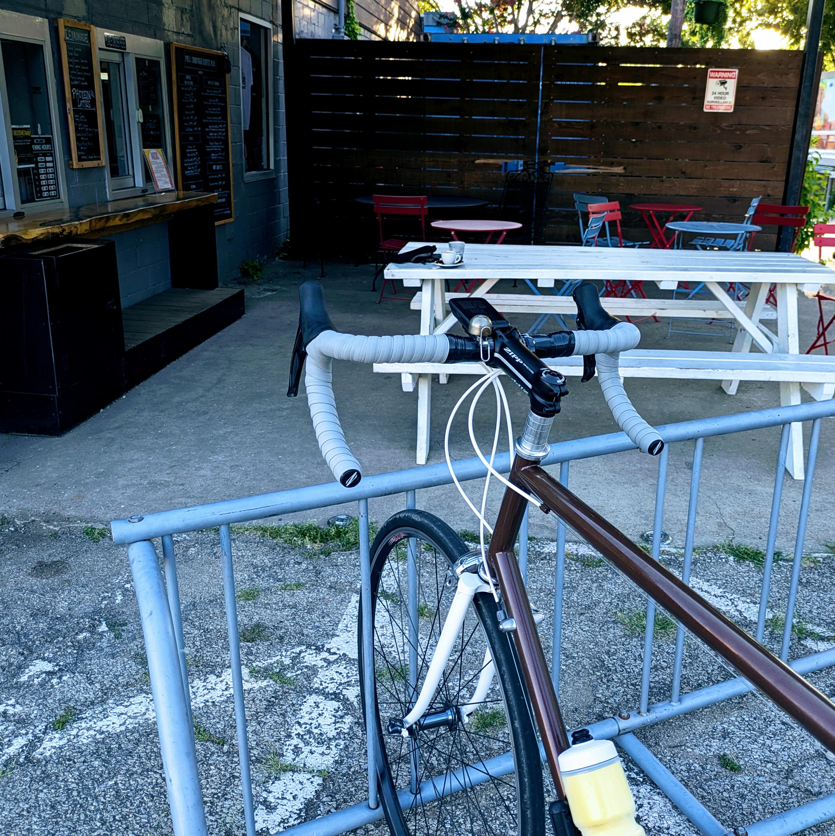 A road bicycle in a bike rack at an outdoor coffee shop