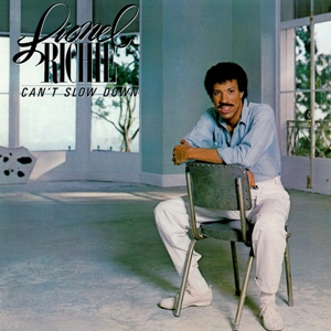 Record cover of "Can't Slow Down" by American recording artist Lionel Richie, released on October 14, 1983, by Motown Records. It's him, sitting in an empty room with big windows in the back--maybe overlooking LA or something, but you can't tell. He's sitting reversed in a chair, like a youth pastor about to get real with the kids. He's wearing a blue oxford shirt with the sleeves slightly rolled up, white pants, and white shoes.