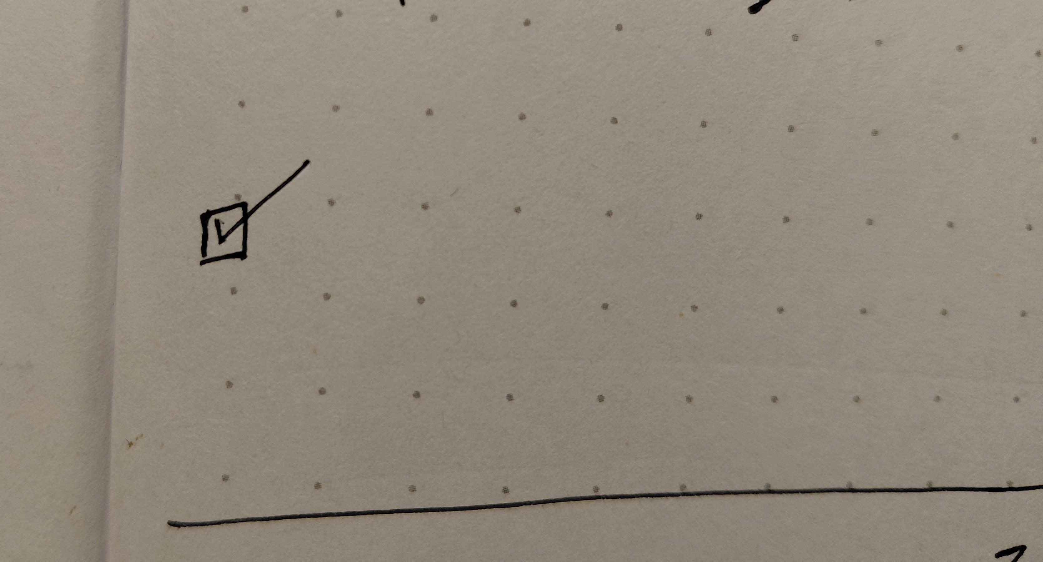 A photo of a portion of a dot grid notebook page with just a checked box with nothing next to it 